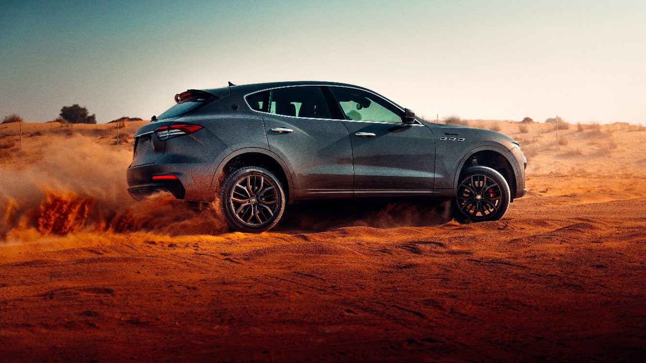 A blue SUV kicking up sand as it drives off-road in the desert.