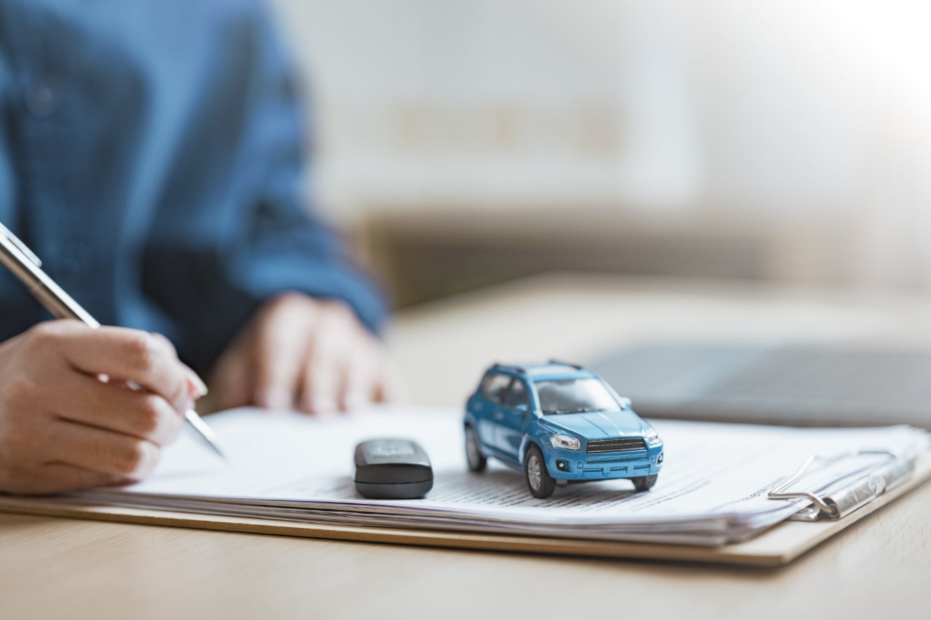 A person signing a vehicle financing deal with a toy blue car and key fob on the document.