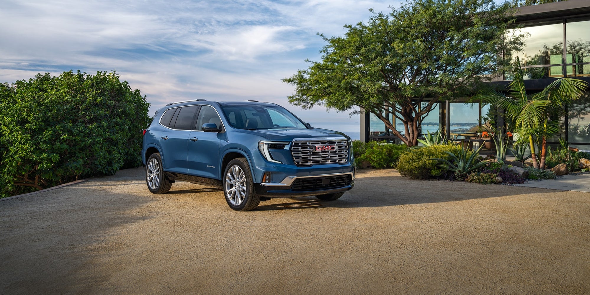 A blue GMC Acadia parked outside a nice house with tropical plants.